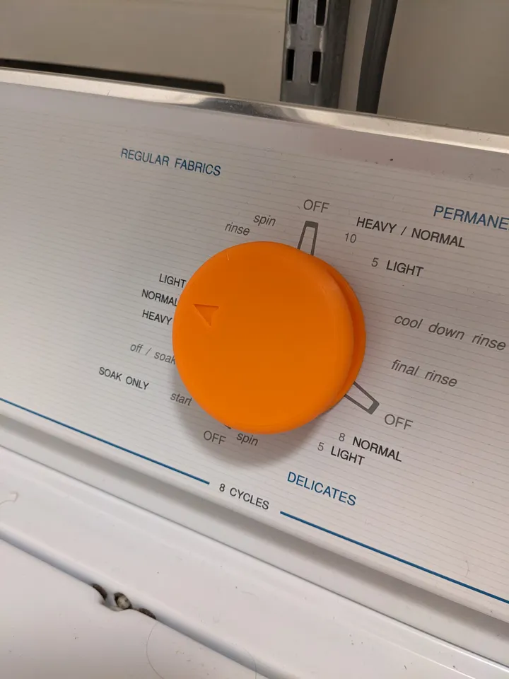 An orange washing machine dial on a white washing machine.
