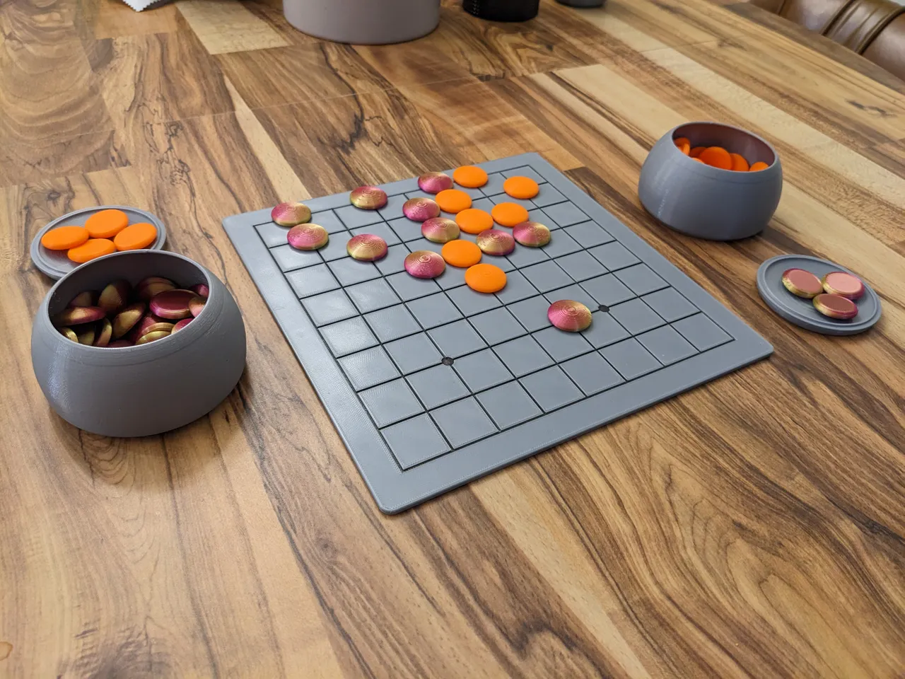 A set of grey Go bowls and a 9x9 Go board with an orange set and a purple set of Go stones.
