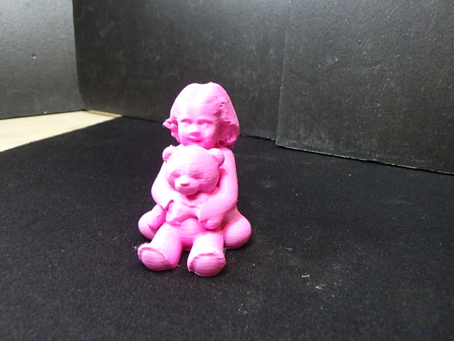 A smiling little girl sitting cross-legged cuddling her teddy bear in dollhouse scale